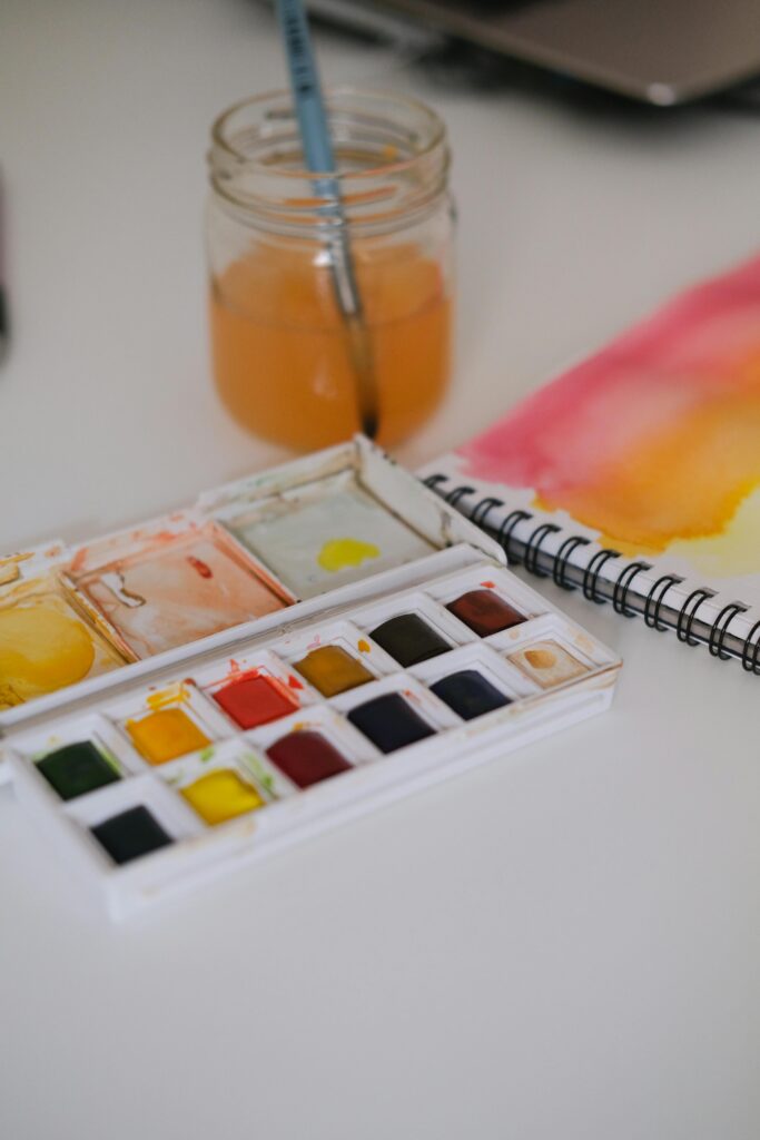 Service-3-min A watercolor paint set with jar and paper on a desk. Perfect for creativity concepts.